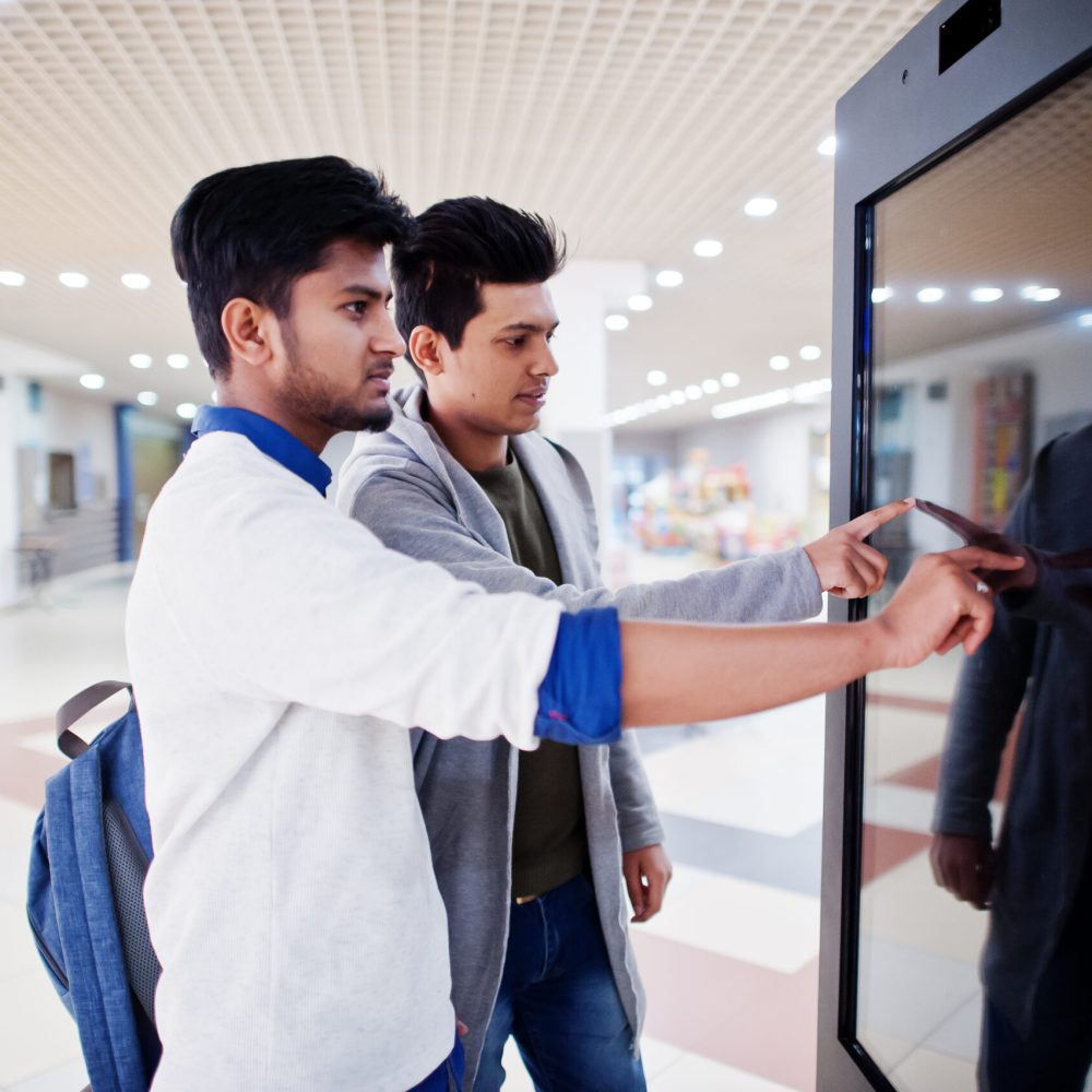 Two asian guys touching screen of electronic information desk in mall.